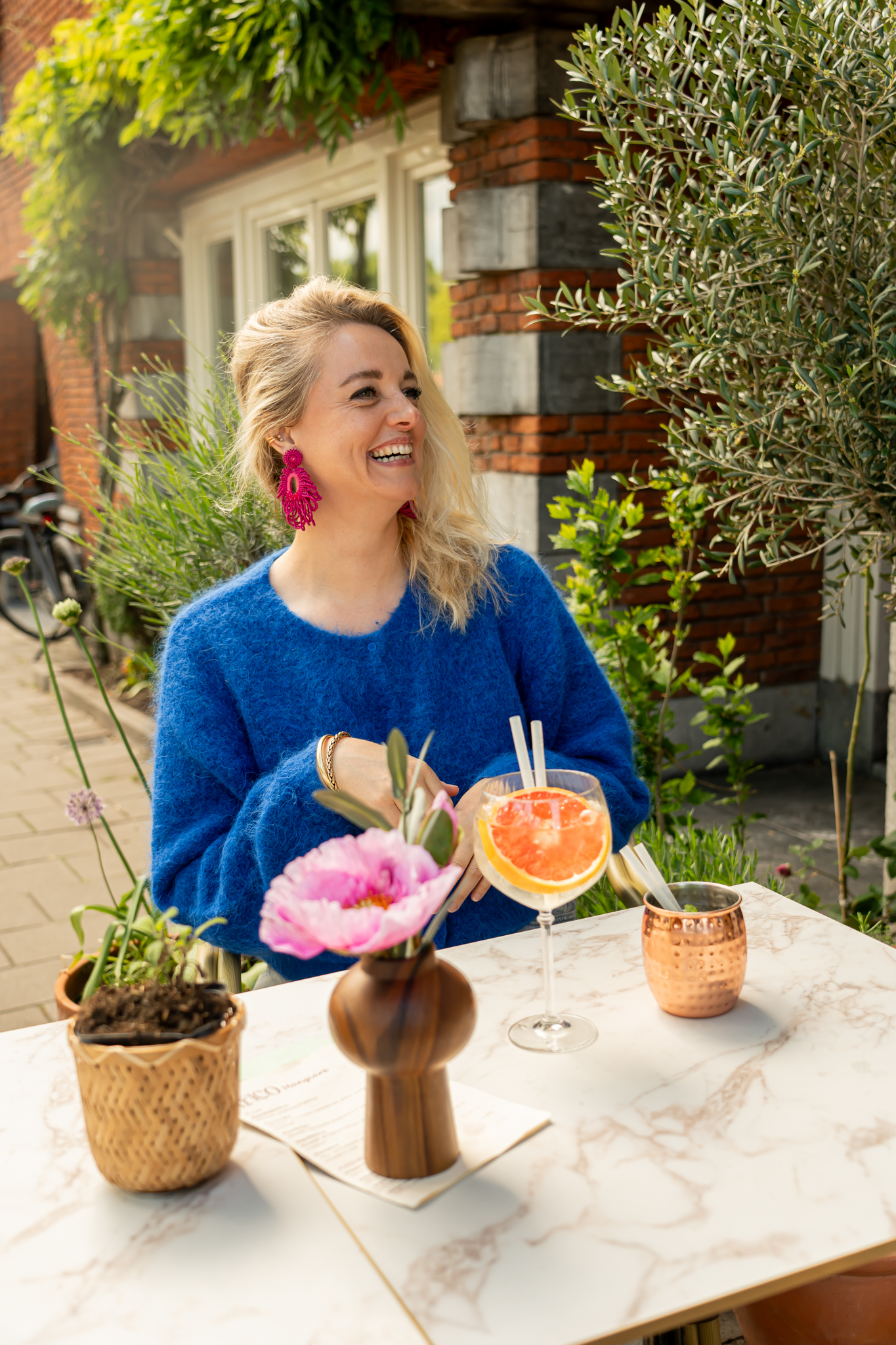 Annejet, eigenaar van Il Fico, lachend aan tafel op het terras met een spritz en bloemen