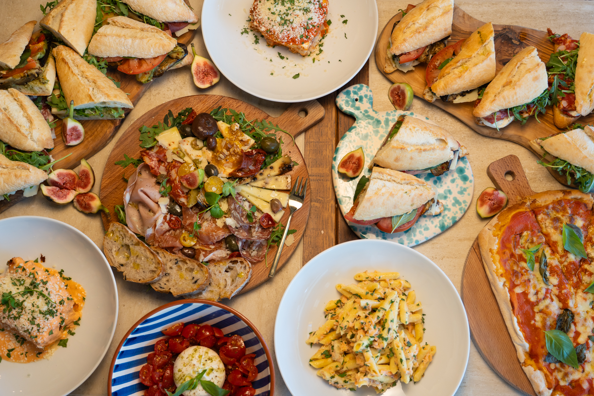 Tafel vol Italiaans eten: panini, een plank met vleeswaren en kaas, pinsa, pastasalade en burrata